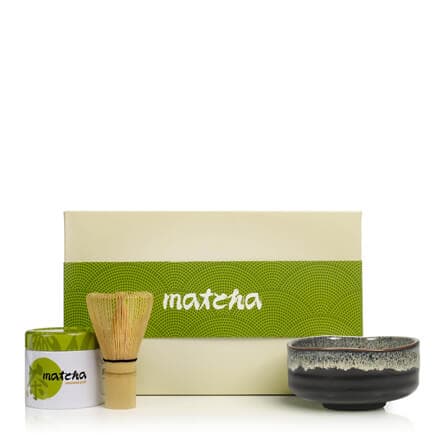 Adagio Teas Matcha Set: green matcha tin, bamboo whisk, and black ceramic bowl in front of a cream gift box on white