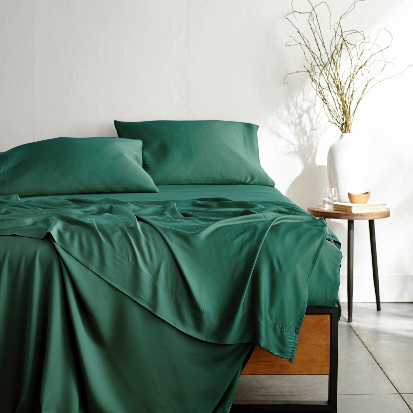 Bamboo Is Better Signature sheet set in emerald green on a low wooden platform bed, two matching pillowcases at the head and the flat sheet hanging over the side