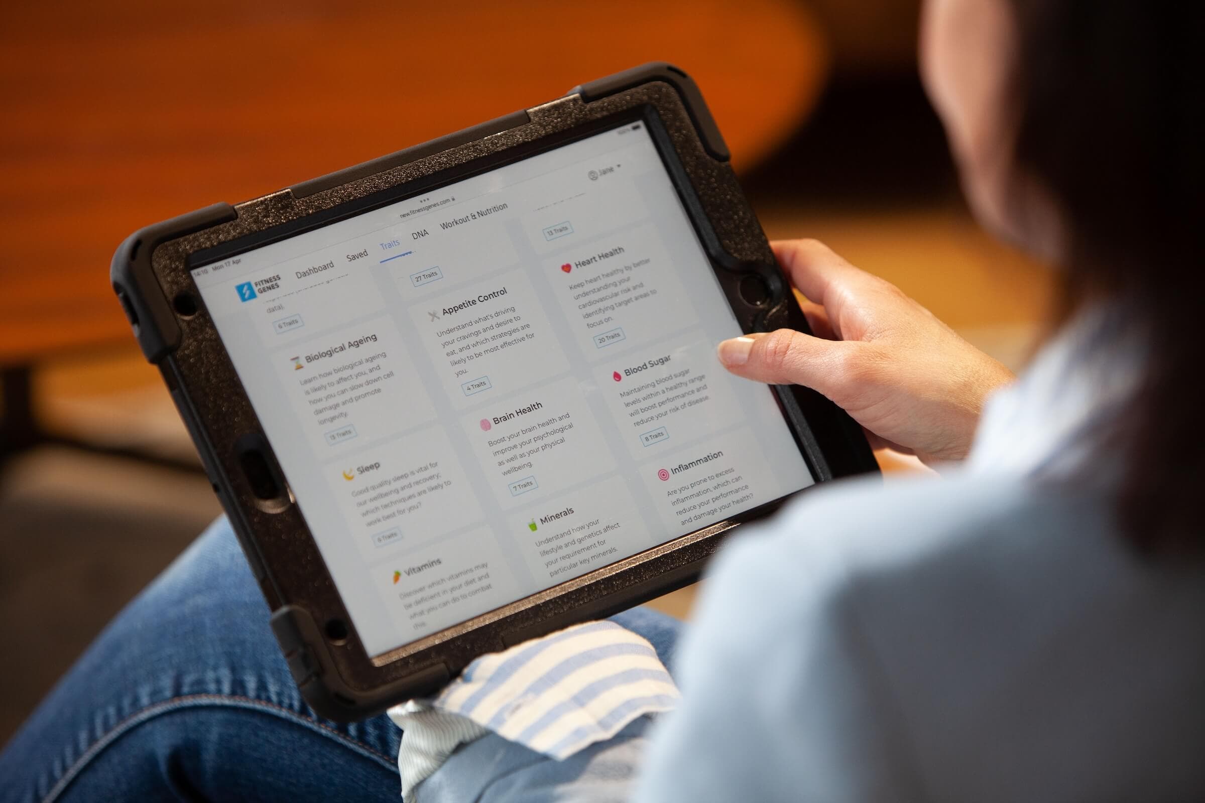 Tablet showing the FitnessGenes reports dashboard with Biological Ageing, Heart Health, Blood Sugar, Sleep and Vitamins traits