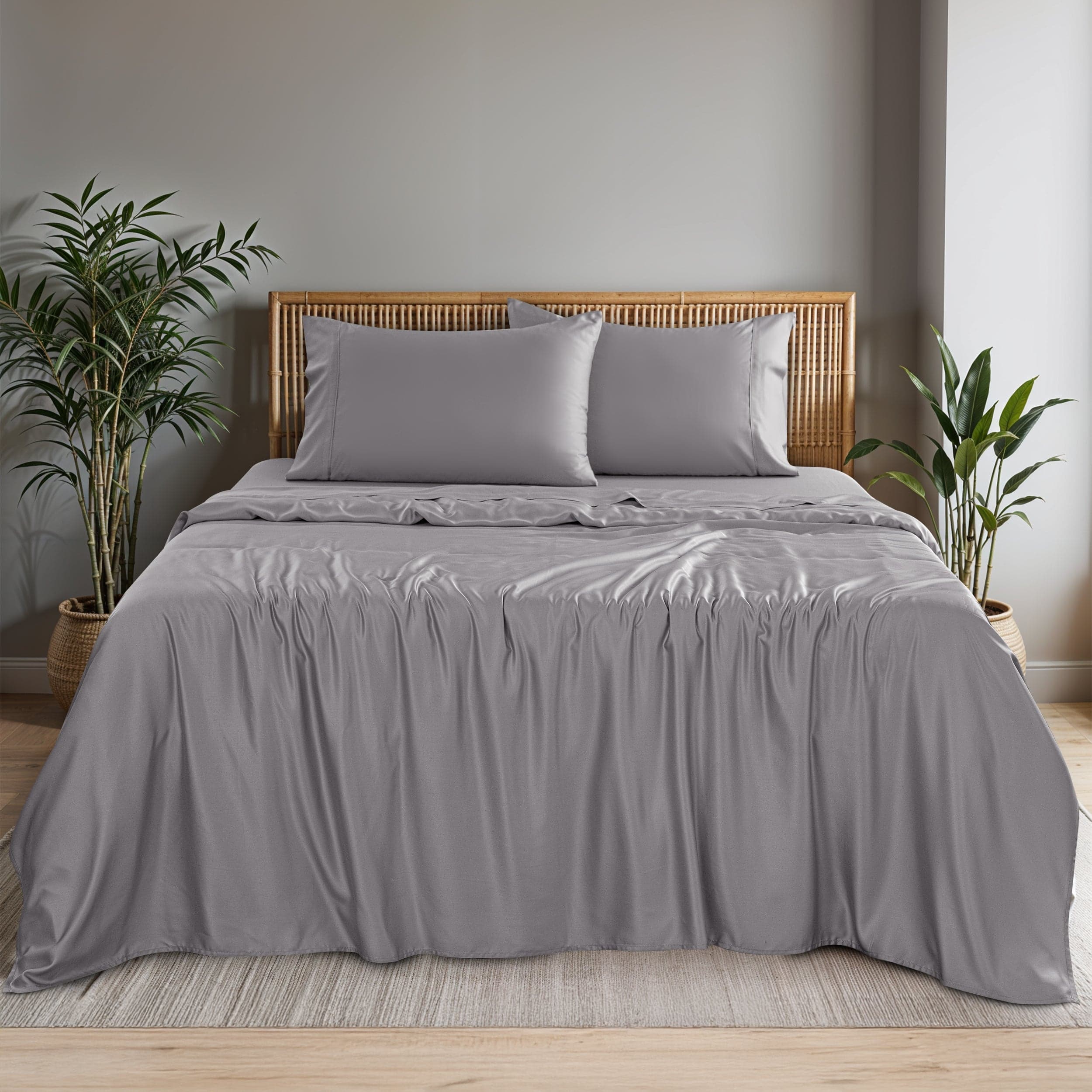 Hannah Linen bamboo viscose sheet set in grey on a made bed, a flat sheet over a fitted sheet and two grey pillowcases against a woven rattan headboard
