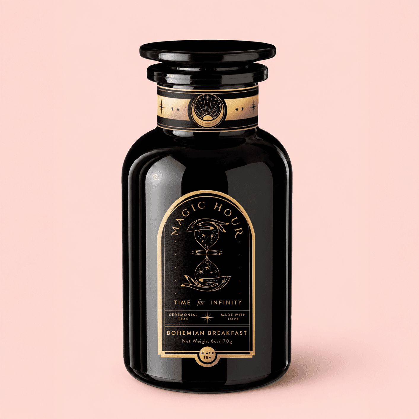 Magic Hour Bohemian Breakfast black tea in a black glass apothecary jar with a stacked lid and a gold label, on a pale pink background