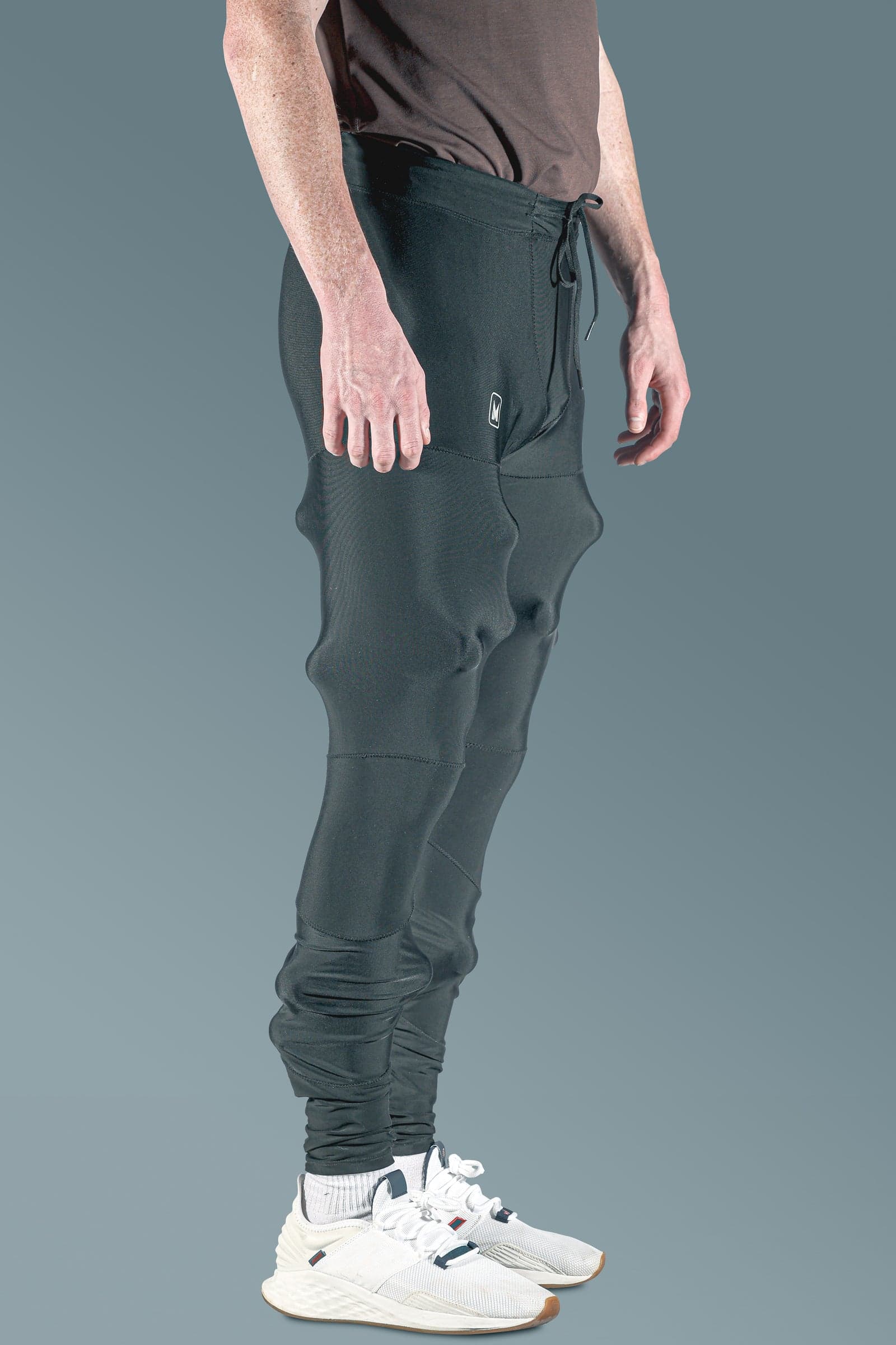 Black drawstring compression pants with raised panels at the thigh, knee and calf, worn by a standing model, side view