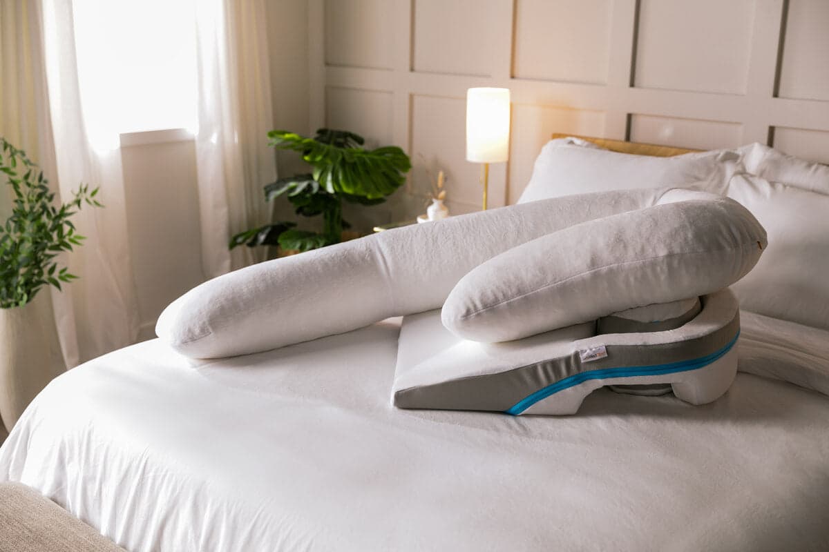 MedCline Shoulder Relief System foam wedge with arm pocket and long white body pillow on a bed