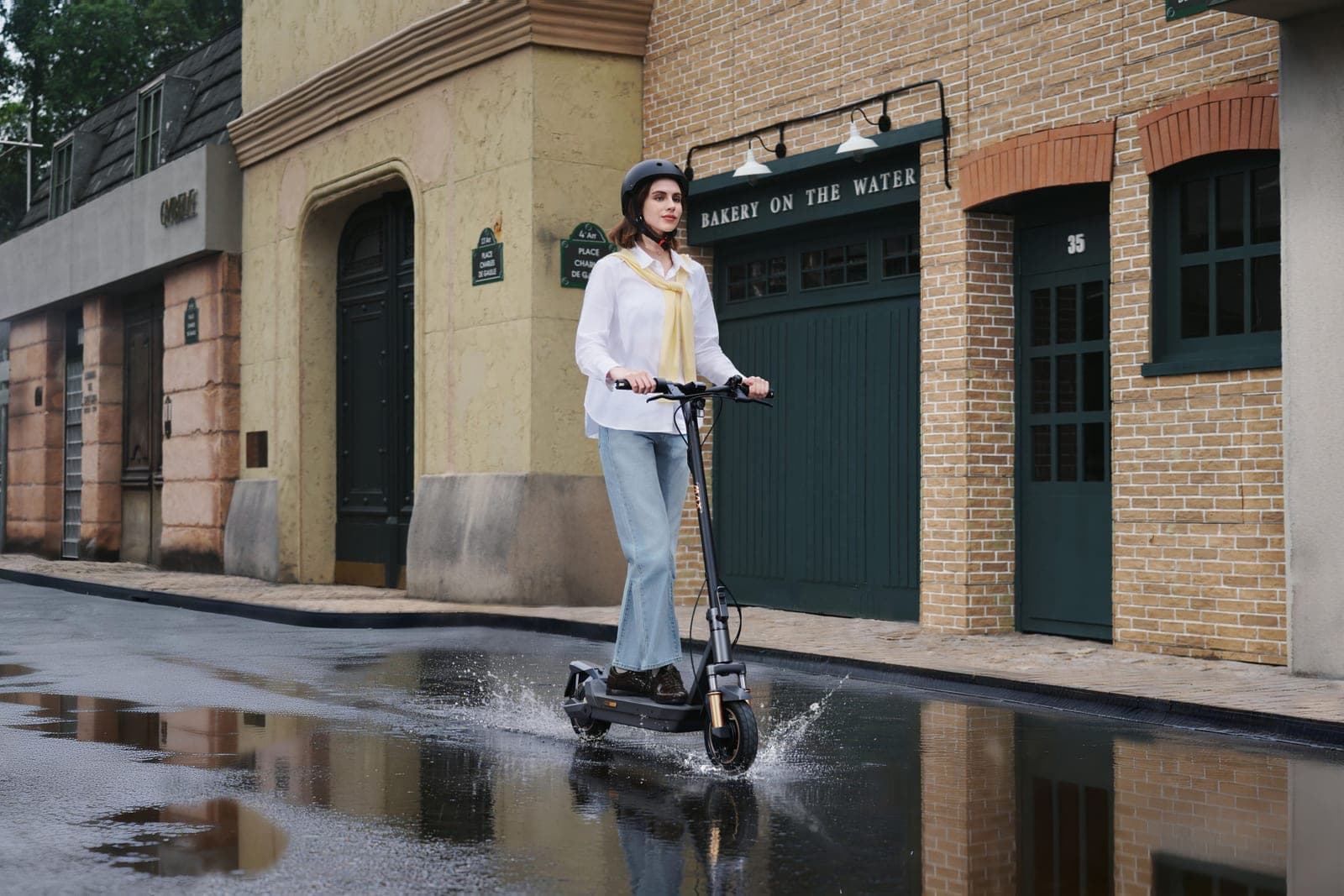 Navee GT5 Max electric scooter ridden through standing water on a wet street, with the front suspension fork and tyre in view