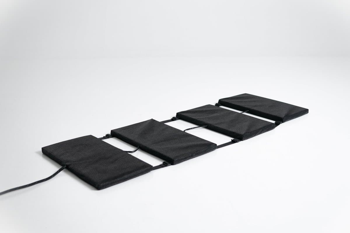 Neurosonic Harmonia laid out flat on a white background: 4 black padded rectangular panels joined in a row by straps, with the power cable leaving the nearest panel
