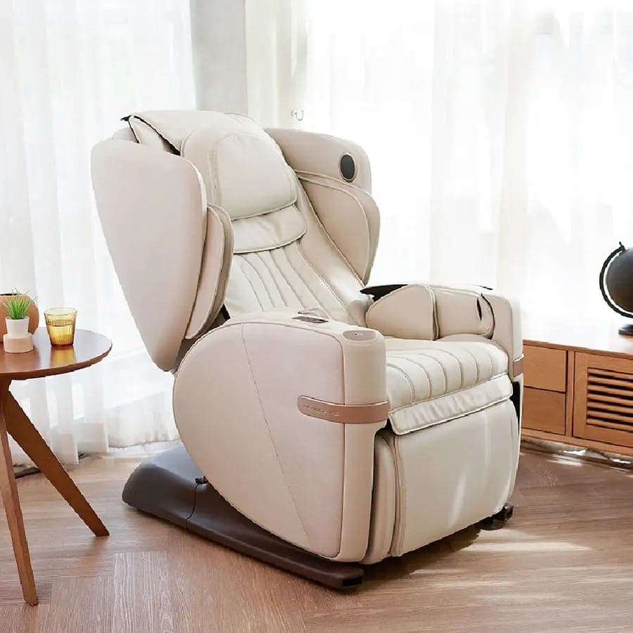 OSIM uDivine V3 massage chair in beige, upright, in a three-quarter view beside a round wooden side table, with sheer curtains behind