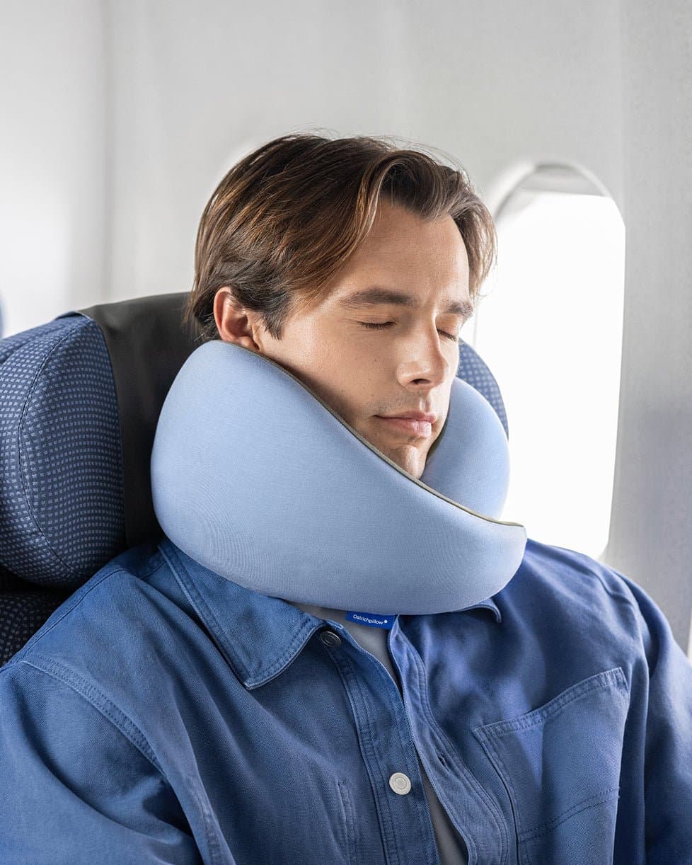 Ostrichpillow Go Neck Pillow in grey memory foam worn around a traveler's neck