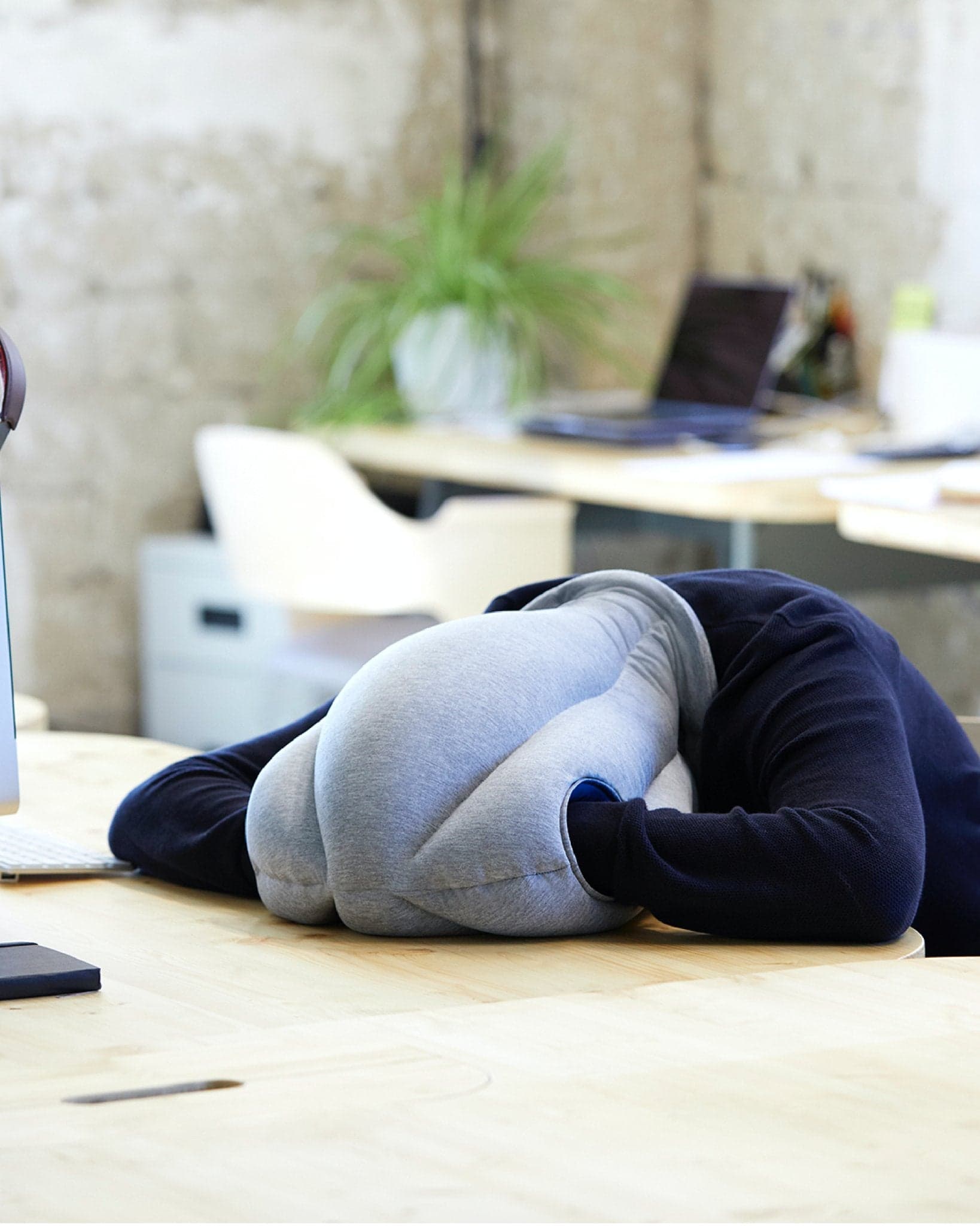 Ostrichpillow Original Napping Pillow worn over the head while resting on a desk