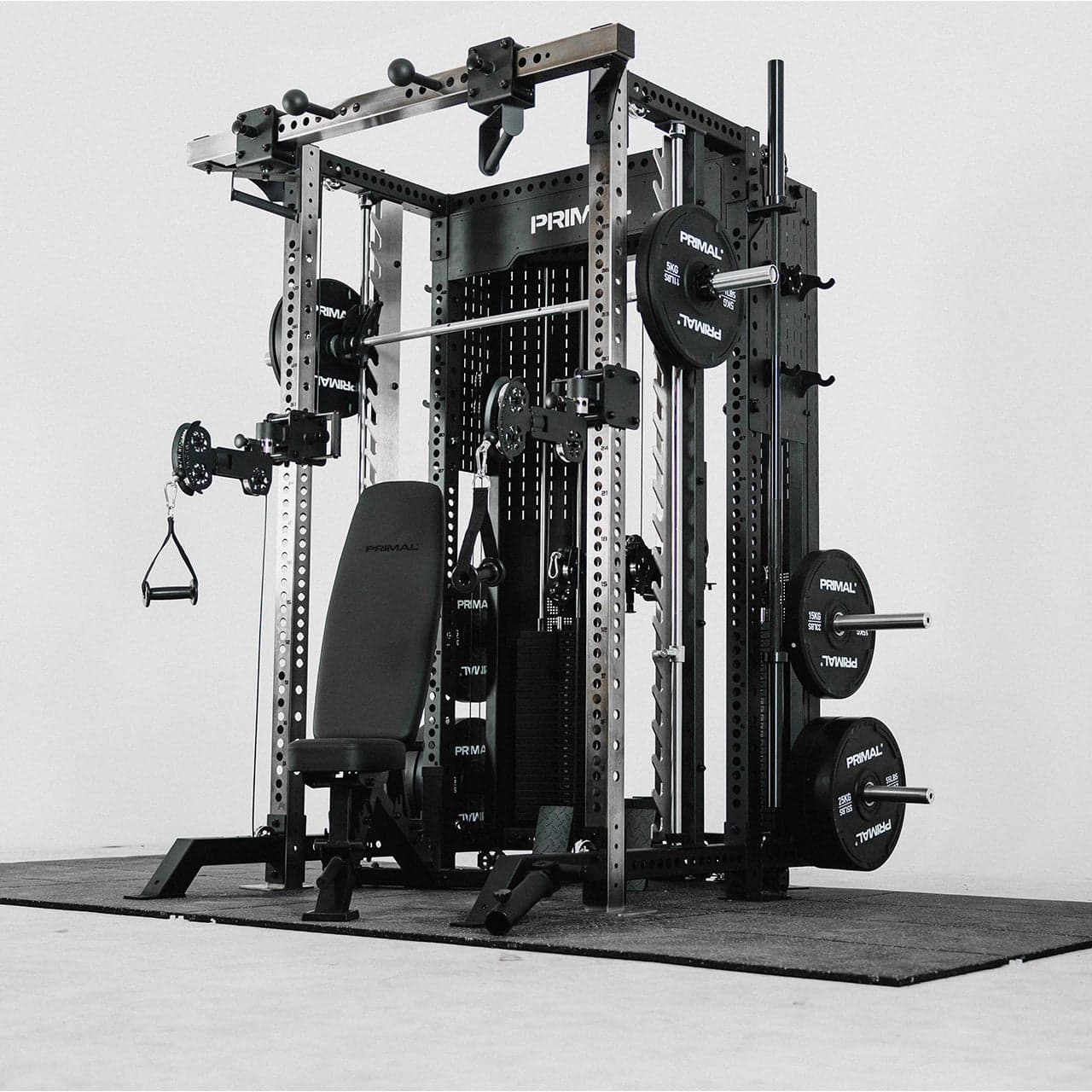 Primal Strength MRX 9.0 multi rack system: black and steel half rack with Smith machine bar, dual pulley arms, an adjustable bench, weight stacks behind the uprights and bumper plates stored on the posts